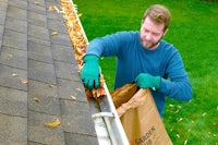 a man cleaning gutters with a bag of leaves