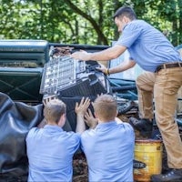 a group of men working on a car in a wooded area